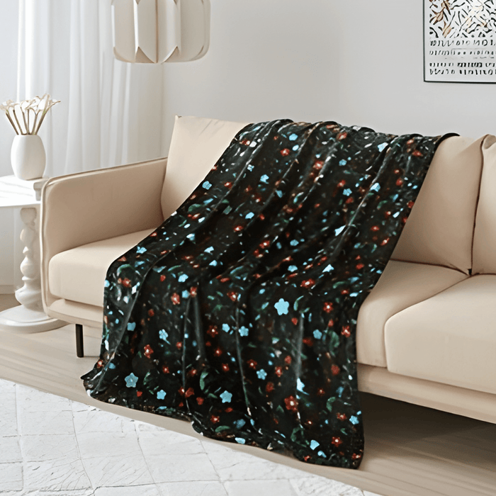 Anishinaabe Enchantment Throw Blanket draped over a couch, featuring traditional floral designs on a dark background.