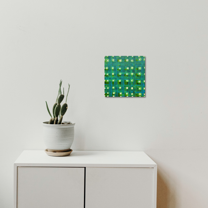 Composition No. 238 by Raul Ortiz features a vibrant geometric grid pattern in emerald green and turquoise hues with raised circular elements, mounted above a white cabinet with a potted cactus plant. The 12x12 inch acrylic on linen artwork creates a striking modern focal point against the minimalist white wall.