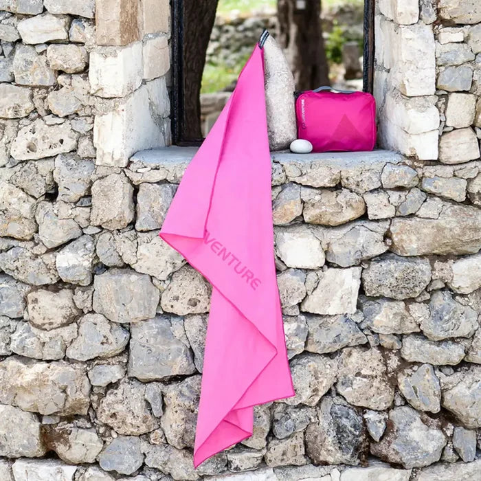 Lifestyle image of a Lifeventure SoftFibre travel towel in xlarge pink hung up to dry on a stone wall