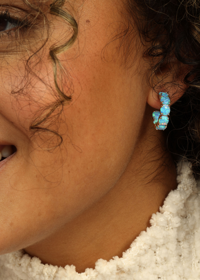 Woman wearing blue opal hoop earrings that are silver framed