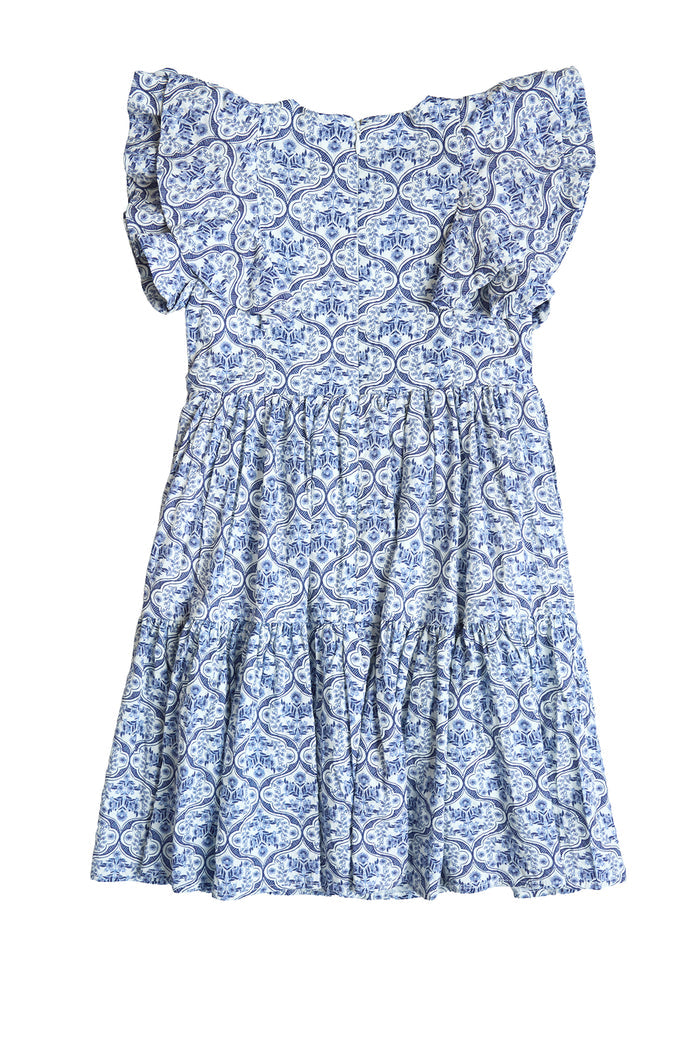The Ivy City Co Mini Trixie Dress in Blue Moroccan Tile features a blue and white paisley pattern, ruffled neckline, and tiered skirt, shown laid flat on a white background.