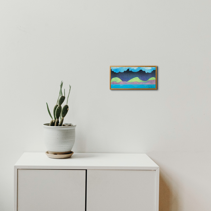 The artwork 'Muffled Saxophone' by Evan Peltzman features an abstract landscape composition with turquoise clouds and coral-colored mountains, framed in wood. The minimalist artwork hangs above a white cabinet with a potted cactus, creating a serene contemporary setting.