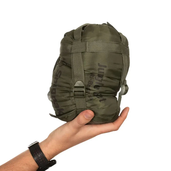 Snugpak Jungle Blanket in olive green packed in its compression stuffsack and held in someones hand on a white background