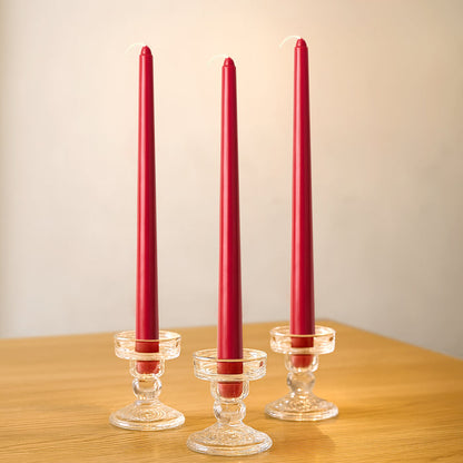Three red taper candles in elegant glass holders on a wooden table.