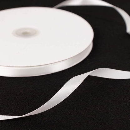 White satin ribbon on a black surface, elegantly curved.