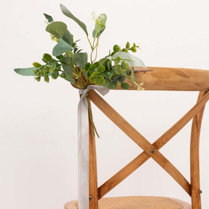 Decorative greenery arrangement on a wooden chair back with ribbon.