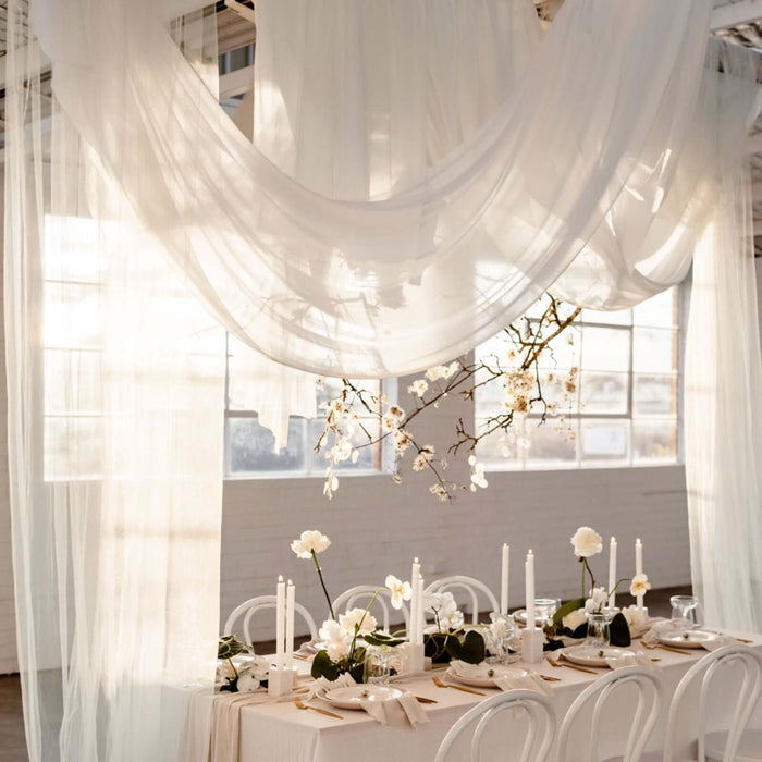 Elegant wedding table setup with draped fabric and floral arrangements in soft lighting.