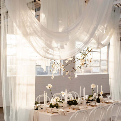 Elegant wedding table setup with draped fabric and floral arrangements in soft lighting.
