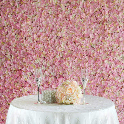 Wedding table setting with champagne flutes and floral centerpiece against pink petal backdrop.
