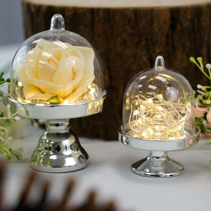 Decorative glass domes with a rose and fairy lights on silver bases.