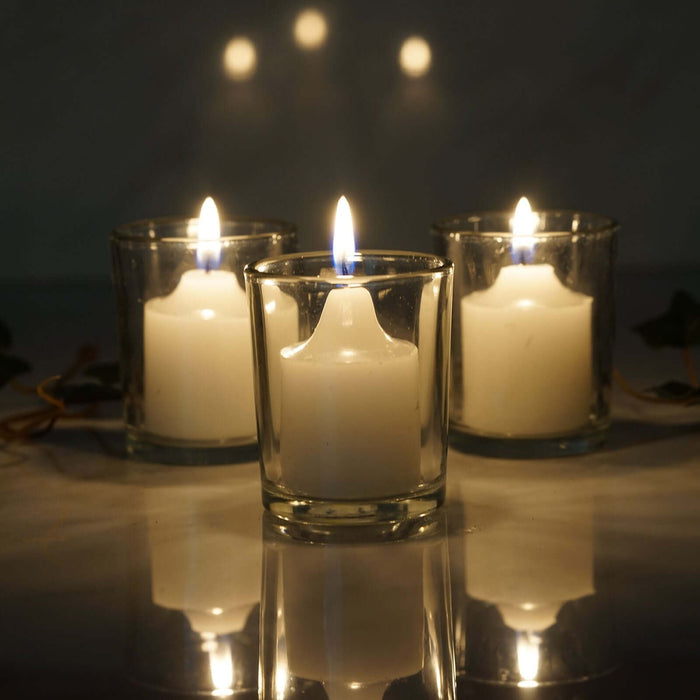 Three glowing white candles in glass holders with a soft reflection.