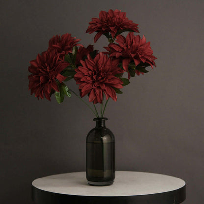 Red artificial flowers in a black vase on a round table.