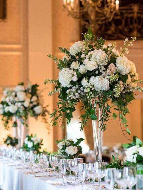 Elegant floral centerpieces with white roses and greenery at a wedding reception.