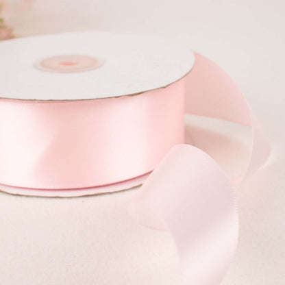 Pink satin ribbon on a spool with loose ribbon flowing off the edge.