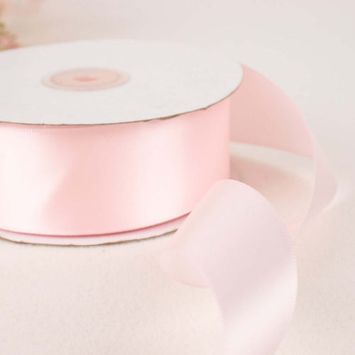 Pink satin ribbon on a spool with loose ribbon flowing off the edge.
