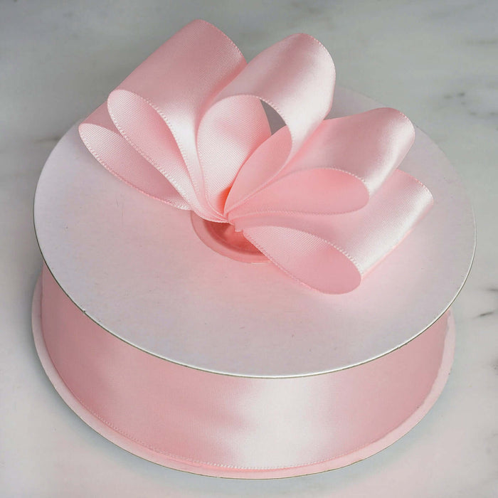 Pink satin ribbon spool with a decorative bow on top.