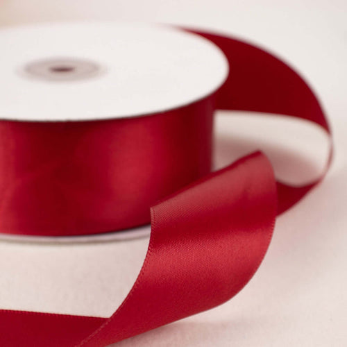 Red satin ribbon on a spool with a flowing tail.