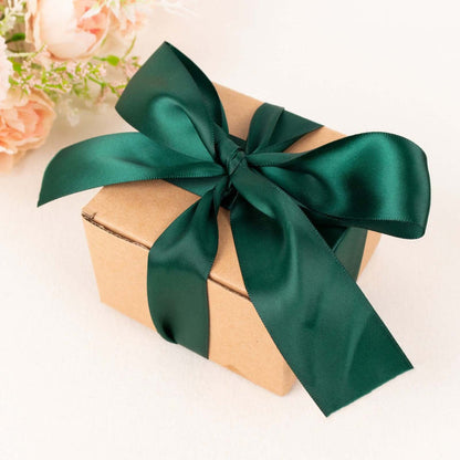 Gift box with green satin ribbon and flowers in the background.