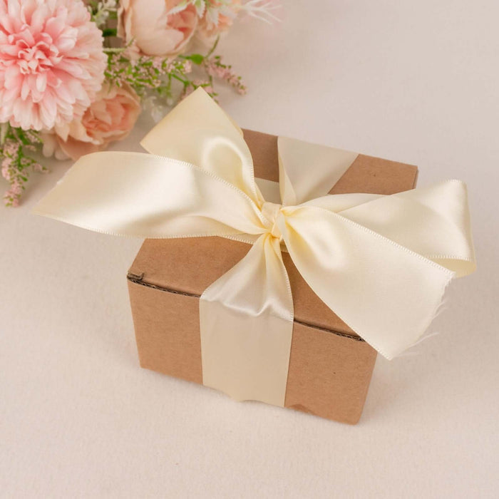 Brown gift box with cream ribbon and floral arrangement in background.