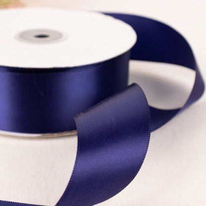 Navy blue satin ribbon roll with a flowing ribbon end.