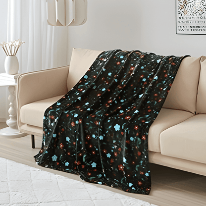 Anishinaabe Enchantment Throw Blanket draped over a couch, featuring traditional floral designs on a dark background.