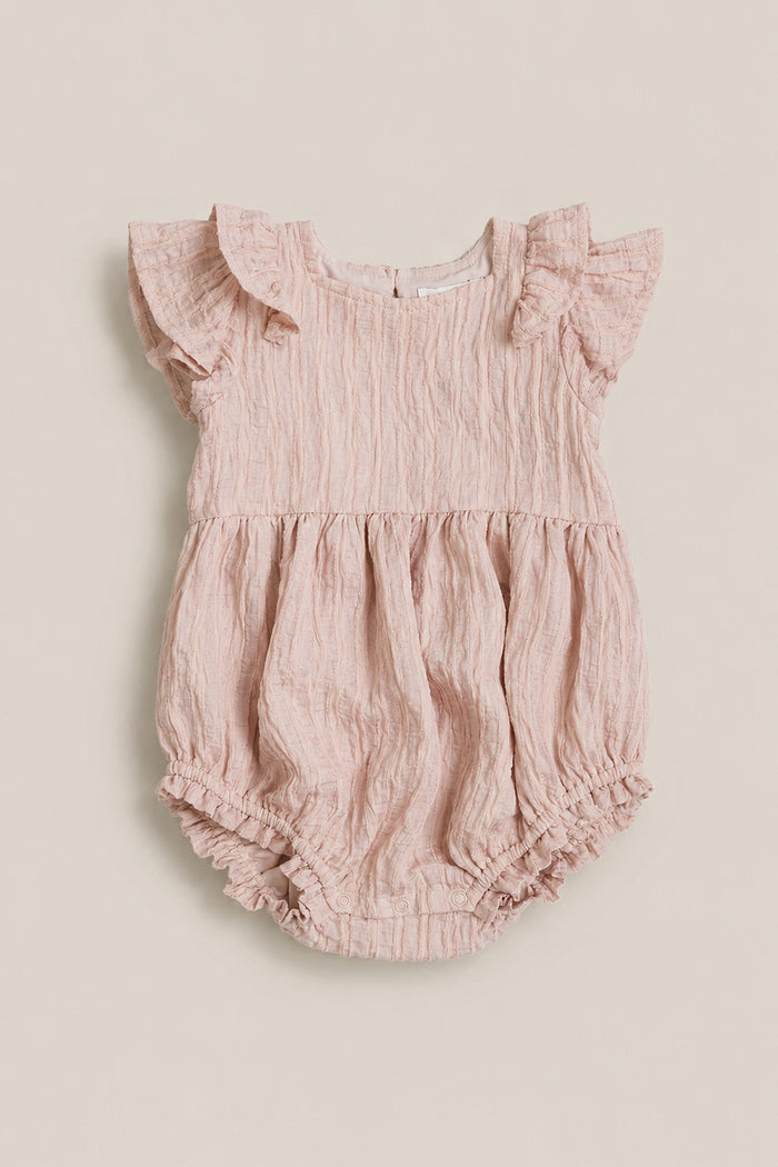 The Ivy City Co Baby Hattie Romper in Pink Stripes features short sleeves with ruffled shoulders, a gathered waist, and elastic leg openings in crinkled fabric. Displayed on a neutral background.