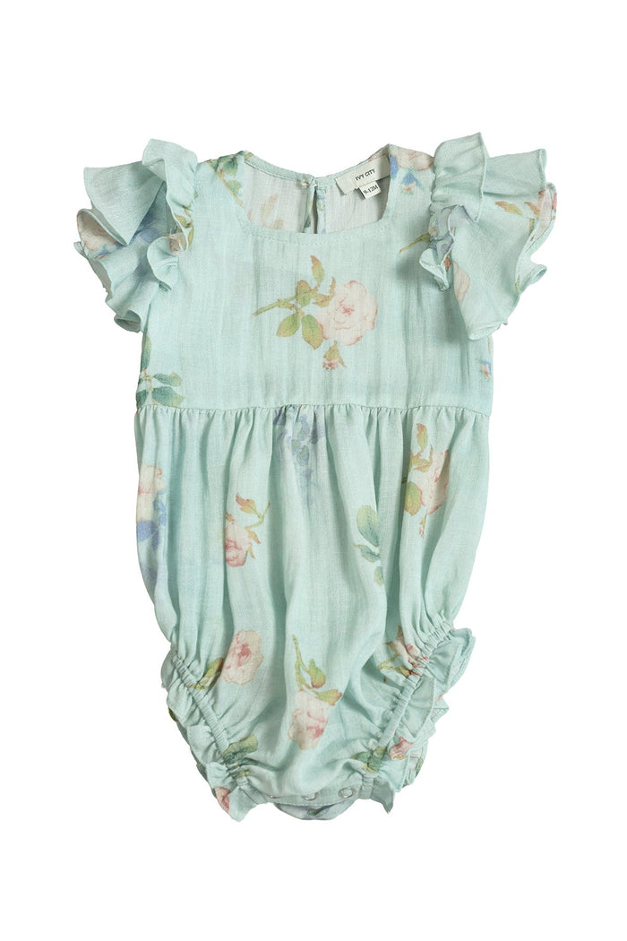 The Ivy City Co Baby Hattie Romper in Roselyn Blue features short, ruffled sleeves and a pastel floral pattern on a light blue background, with gentle gathering at the legs and waist. Displayed on a white background, this darling piece is perfect for coordinating mommy-and-me outfits.