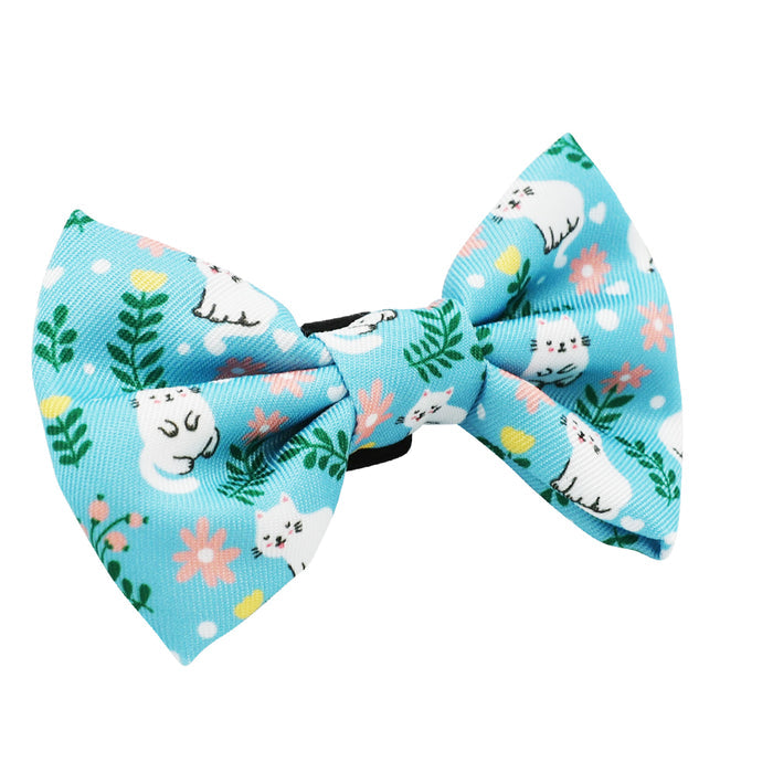 The Sassy Woof Cat Bowtie - Purrs & Petals features white cartoon cats, green leaves, and pink and yellow flowers on a light blue polka dot background. Pair it with an adjustable harness or matching leash for a complete look.