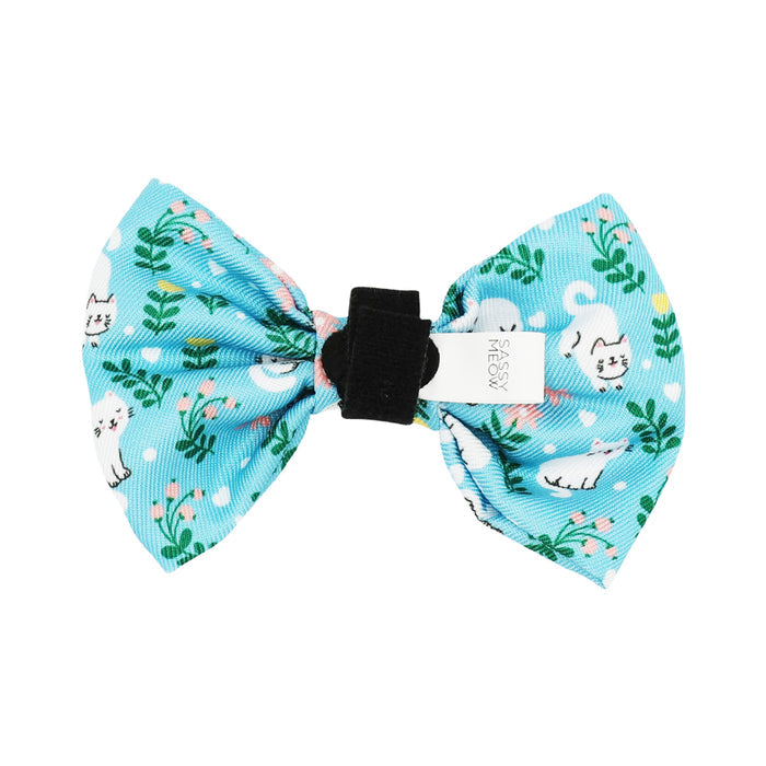 The Sassy Woof Cat Bowtie - Purrs & Petals is a light blue bowtie for cats with a black center, white cat illustrations, green plants, pink flowers, and a small white tag. Pair with the matching leash or adjustable harness for a coordinated style.