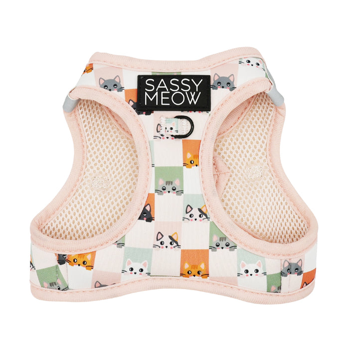 The Cat Step-In Harness - Smitten Kittens by Sassy Woof features a pastel pink grid pattern with colorful cartoon cat faces and displays a black "Sassy Woof" tag at the top.