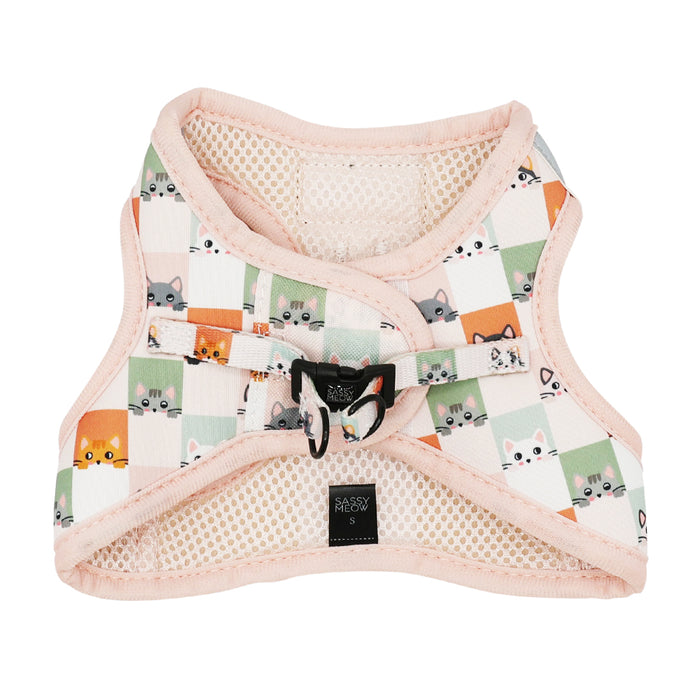 The Cat Step-In Harness - Smitten Kittens by Sassy Woof features a pastel pink and cream checkered pattern with cartoon cat faces, a black buckle, mesh lining, reflective strips, and a front Sassy Meow label.