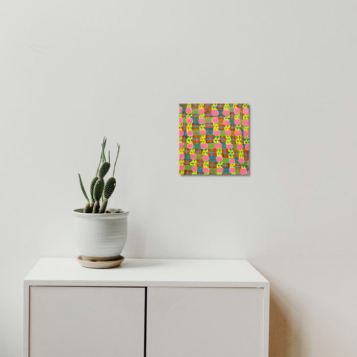 The artwork 'Composition No. 239' by Raul Ortiz features a vibrant grid pattern with interwoven pink, yellow, and green geometric shapes on linen canvas. The abstract composition creates a dynamic interplay of colors and rectangular forms. A 12x12 inch acrylic painting mounted above white furniture with minimalist styling. - By Raul Ortiz
