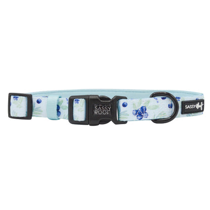 The Sassy Woof Dog Collar - Berry Sassy features a light blue floral pattern, an adjustable fit, a black plastic buckle with the Sassy Woof logo, and a sturdy D-ring for leash attachment.