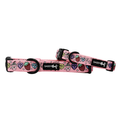 Two Sassy Woof "I Chews You" dog collars, pink and adjustable with black buckles, sturdy D-ring leash attachments, colorful fruit and drink designs, and a black Sassy Woof logo patch on each.