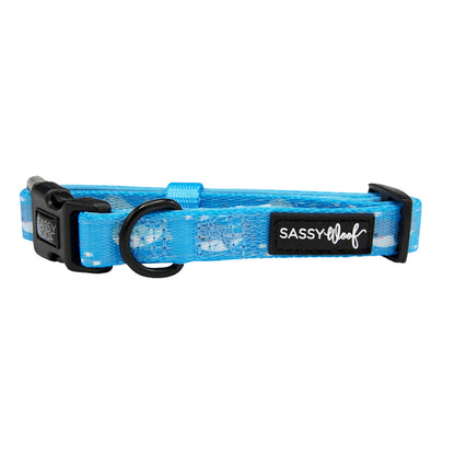 The Sassy Woof “Might as Whale” adjustable dog collar is blue with a white cloud-like pattern, black plastic buckle, metal D-ring, logo tag, and pairs perfectly with the matching neoprene harness.