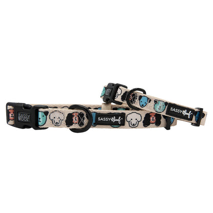 The Sassy Woof “Mixed With Love” dog collar and matching leash are beige with cartoon dog faces in black, white, teal, and tan. Made of comfy neoprene, each has black plastic clasps and a sturdy D-ring for secure attachment.