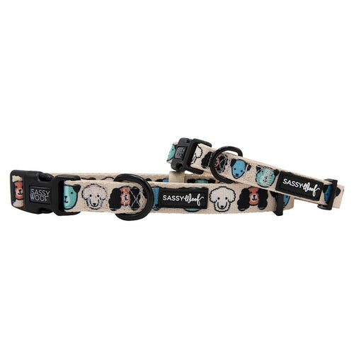 The Sassy Woof “Mixed With Love” dog collar and matching leash are beige with cartoon dog faces in black, white, teal, and tan. Made of comfy neoprene, each has black plastic clasps and a sturdy D-ring for secure attachment.