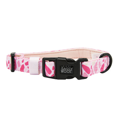 The Sassy Woof Dog Collar - Mykonos features a pink and white pattern, black plastic buckle, black metal ring, and the Sassy Woof logo. This adjustable collar provides comfort and style for your dog.