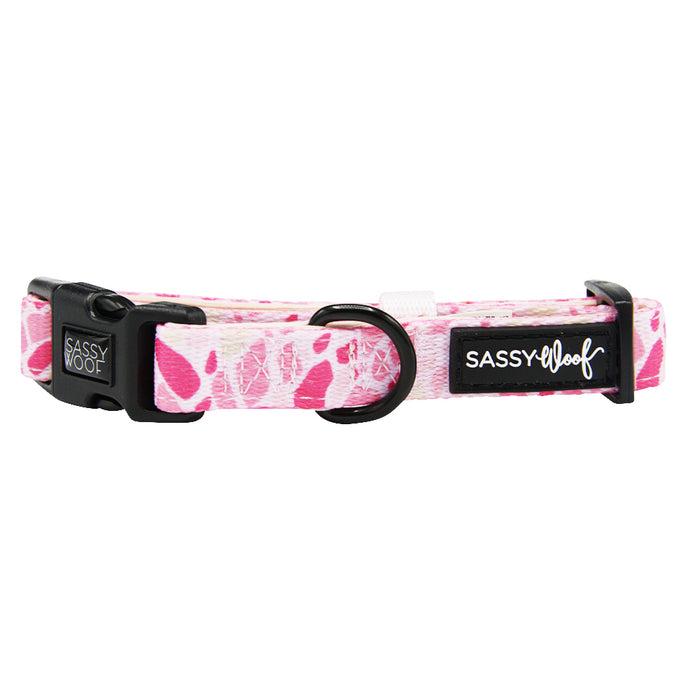 The Dog Collar - Mykonos by Sassy Woof is a pink and white patterned adjustable neoprene collar with a black plastic buckle, metal D-ring, and Sassy Woof branding on a black label.
