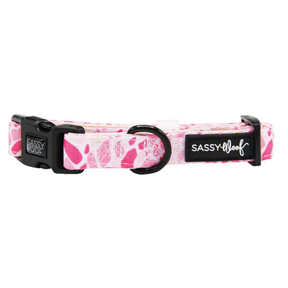 The Dog Collar - Mykonos by Sassy Woof is a pink and white patterned adjustable neoprene collar with a black plastic buckle, metal D-ring, and Sassy Woof branding on a black label.