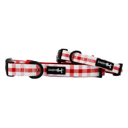 Two Sassy Woof "Dog Collar - Picnic Fur Two" adjustable collars, in red and white plaid with black plastic buckles and sturdy D-rings, are displayed against a white background with Sassy Woof labels on each.