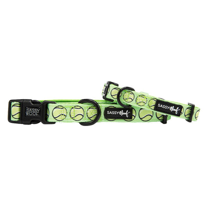 Two green "Serving Up Sass" dog collars by Sassy Woof, featuring tennis ball patterns and black clasps with logo patches, are overlapped in a playful display.