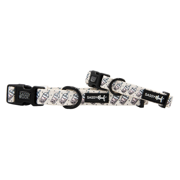 Two adjustable “Spill the Tea” dog collars from Sassy Woof feature sturdy D-rings, black plastic buckles, and white neoprene with a boba tea cup pattern and the Sassy Woof logo.