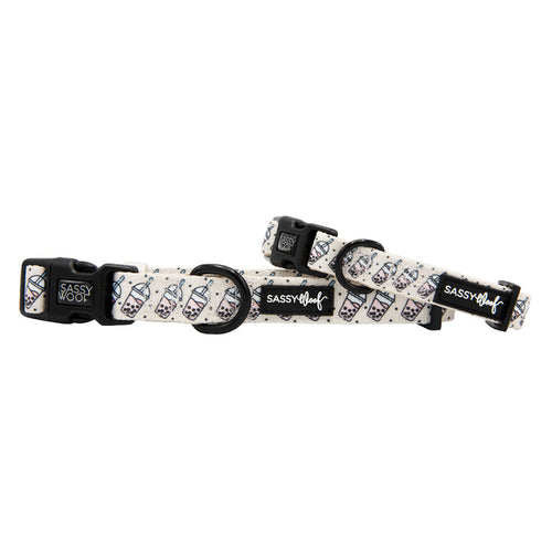 Two adjustable “Spill the Tea” dog collars from Sassy Woof feature sturdy D-rings, black plastic buckles, and white neoprene with a boba tea cup pattern and the Sassy Woof logo.