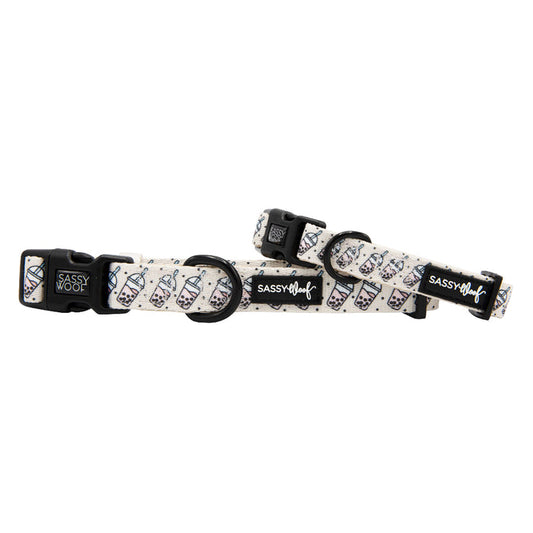 Two adjustable “Spill the Tea” dog collars from Sassy Woof feature sturdy D-rings, black plastic buckles, and white neoprene with a boba tea cup pattern and the Sassy Woof logo.