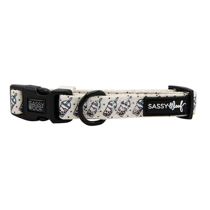 The Sassy Woof "Spill the Tea" dog collar features a beige design with bubble tea cup patterns, black hardware, branded labels on the buckle and strap, and a sturdy D-ring for secure leash attachment.