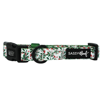 The Sassy Woof Dog Collar - Under the Mistletoe features a green and red foliage pattern, black plastic buckles, a metal ring, and an adjustable fit with a black SASSY WOOF tag—perfect to pair with matching accessories.