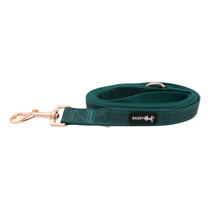 A coiled teal dog leash, part of the Dog Collar Three Piece Bundle - Forest by Sassy Woof, featuring a rose gold metal clip and a SASSY WOOF label on the side, is displayed on a white background.