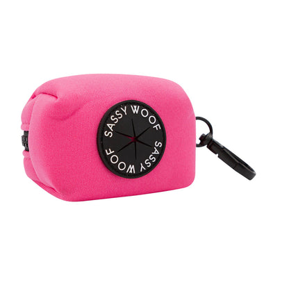 The Sassy Woof Dog Four Piece Bundle in Neon Pink includes a bright pink, rectangular waste bag holder with a black circular dispenser and clip for attaching to leashes, bags, or your matching neon pink harness.