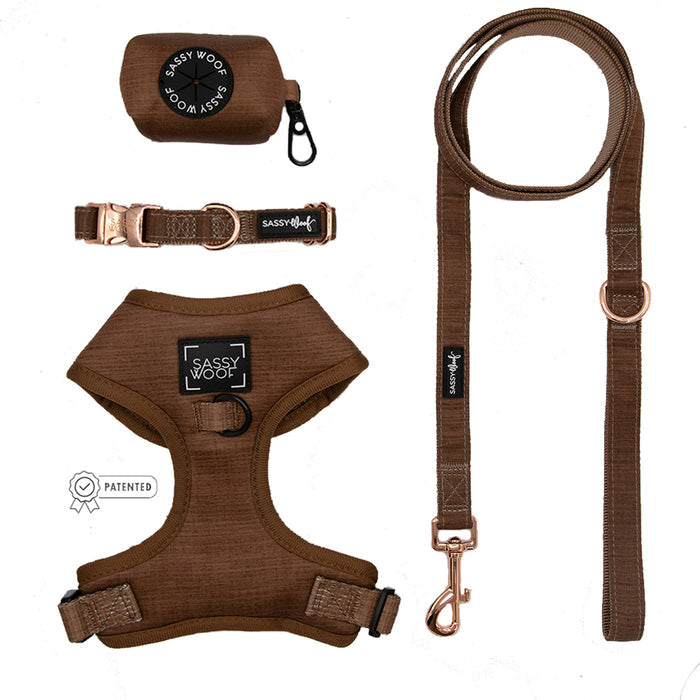 Flat lay of the Sassy Woof Dog Four Piece Bundle - Teddy: adjustable harness with logo patch, leash, collar, and waste bag holder—all in matching brown fabric with rose gold hardware.